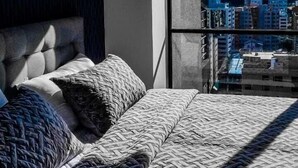 A bedroom with a large bed, a view of a cityscape through a window, and a hanging light fixture. - Luxury apartments Quito (Quito)