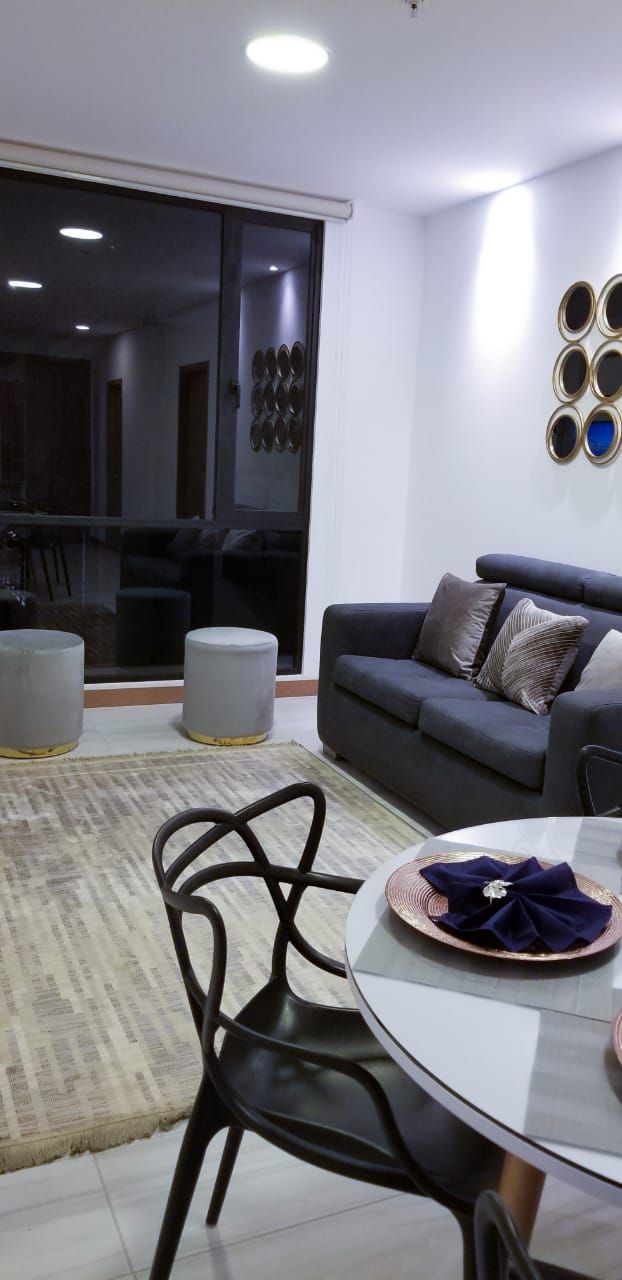 A modern living room with a grey sofa, a round glass table, and a black chair.