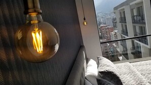 A modern bedroom with a large window, a hanging light bulb, and a view of the cityscape. - Luxury apartments Quito (Quito)