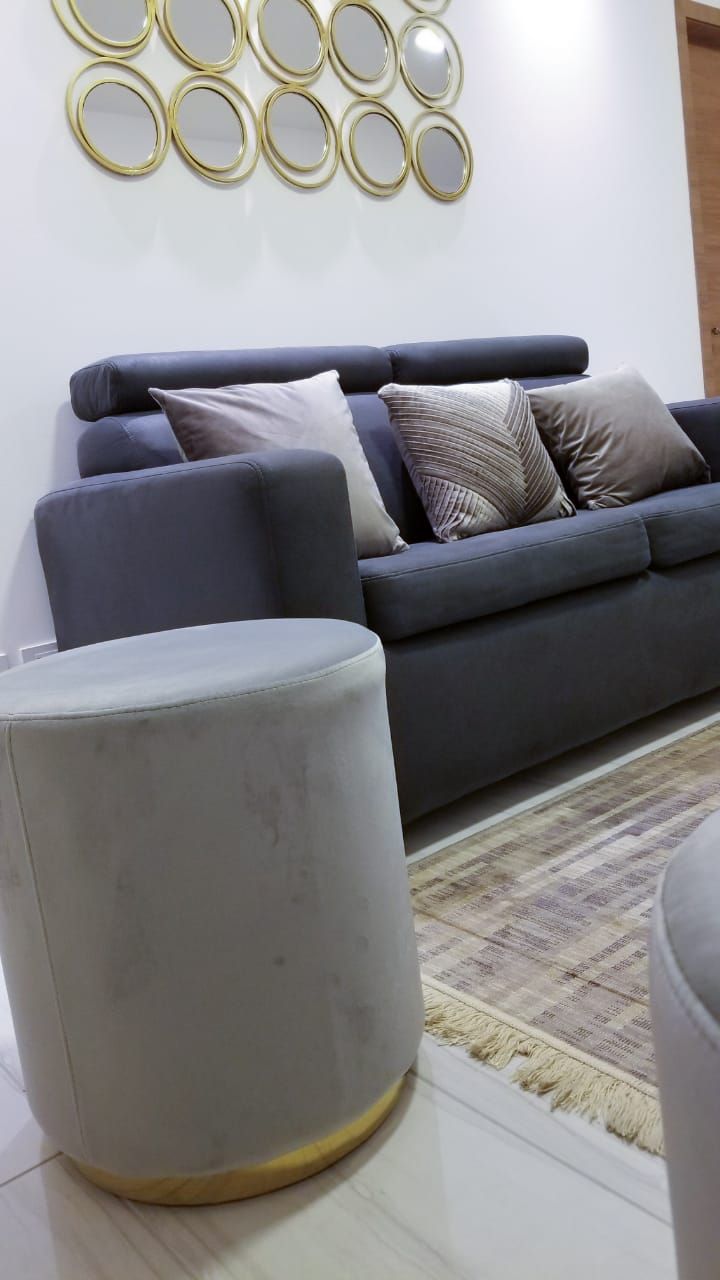 A living room with a grey sofa, multiple cushions, a grey ottoman, and a wall-mounted circular mirror arrangement.