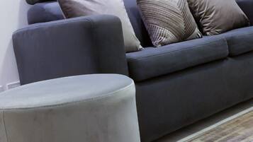 A living room with a grey sofa, multiple cushions, a grey ottoman, and a wall-mounted circular mirror arrangement.