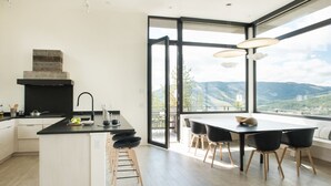 A modern kitchen with a large island, black bar stools, and a dining area with black chairs. - Lone Peak Views | Hot Tub | Ski-In/Out (Big Sky)
