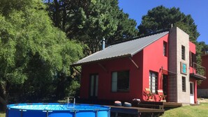 Una casa rossa con una piscina blu e un patio.