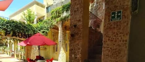 An outdoor seating area with stone columns, red umbrellas, and a staircase leading to an upper level.