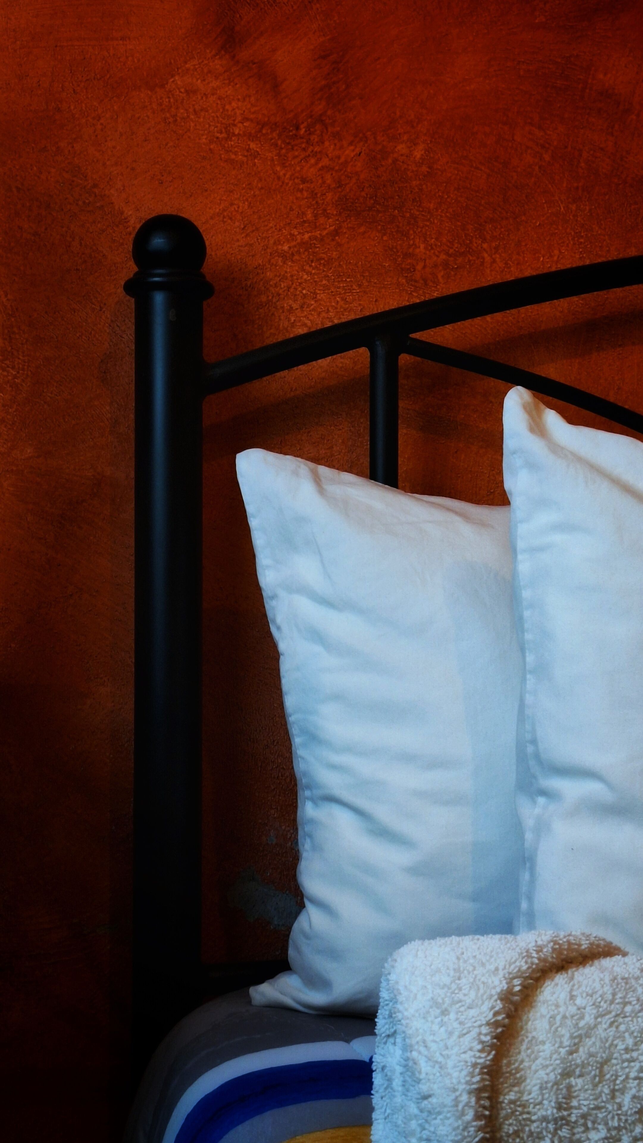 A bed with a black metal frame and white pillows against a textured orange wall.