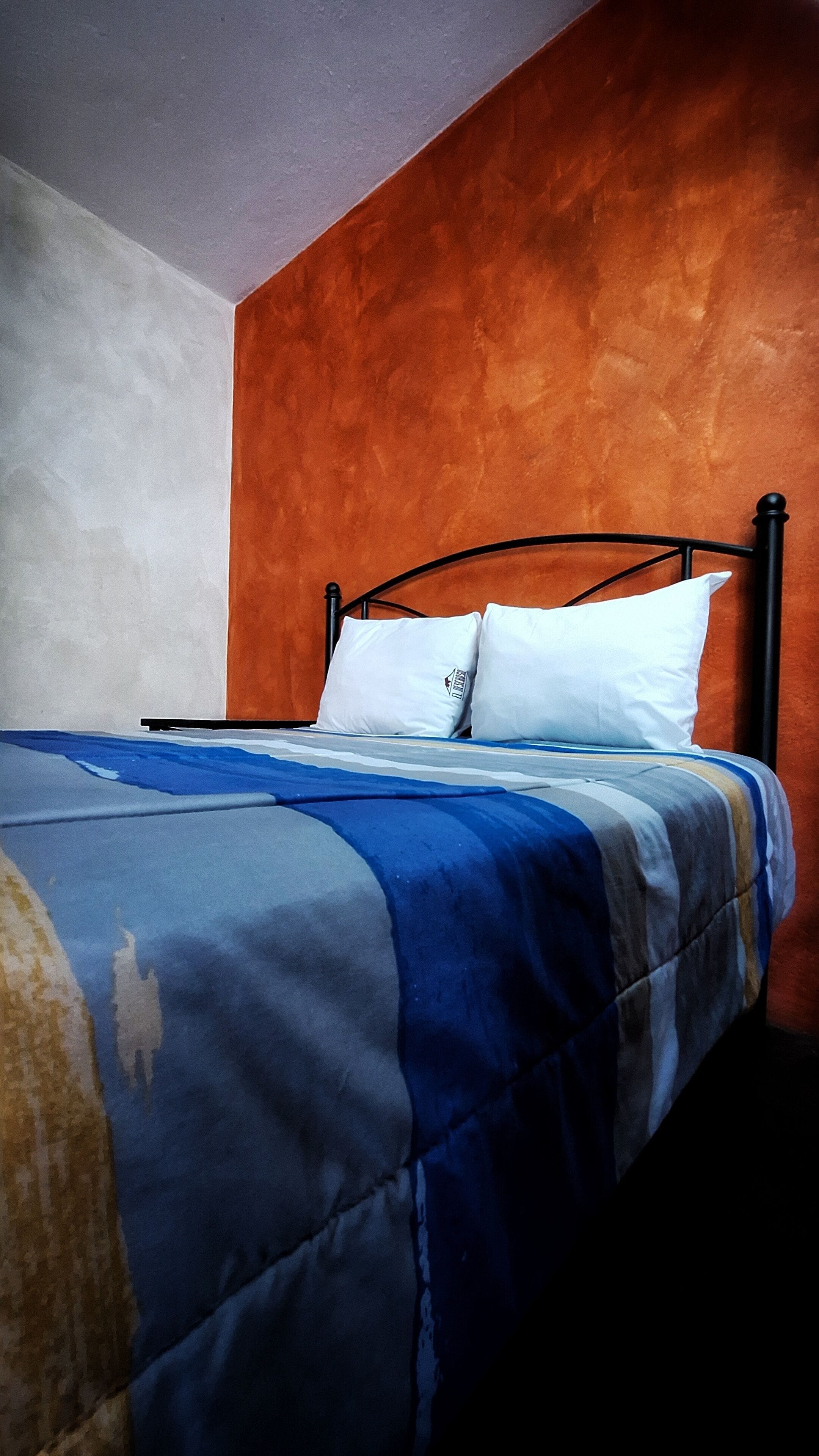 A bed with a blue and white striped bedspread, a white pillow, and a black metal headboard in a room with orange and white walls.