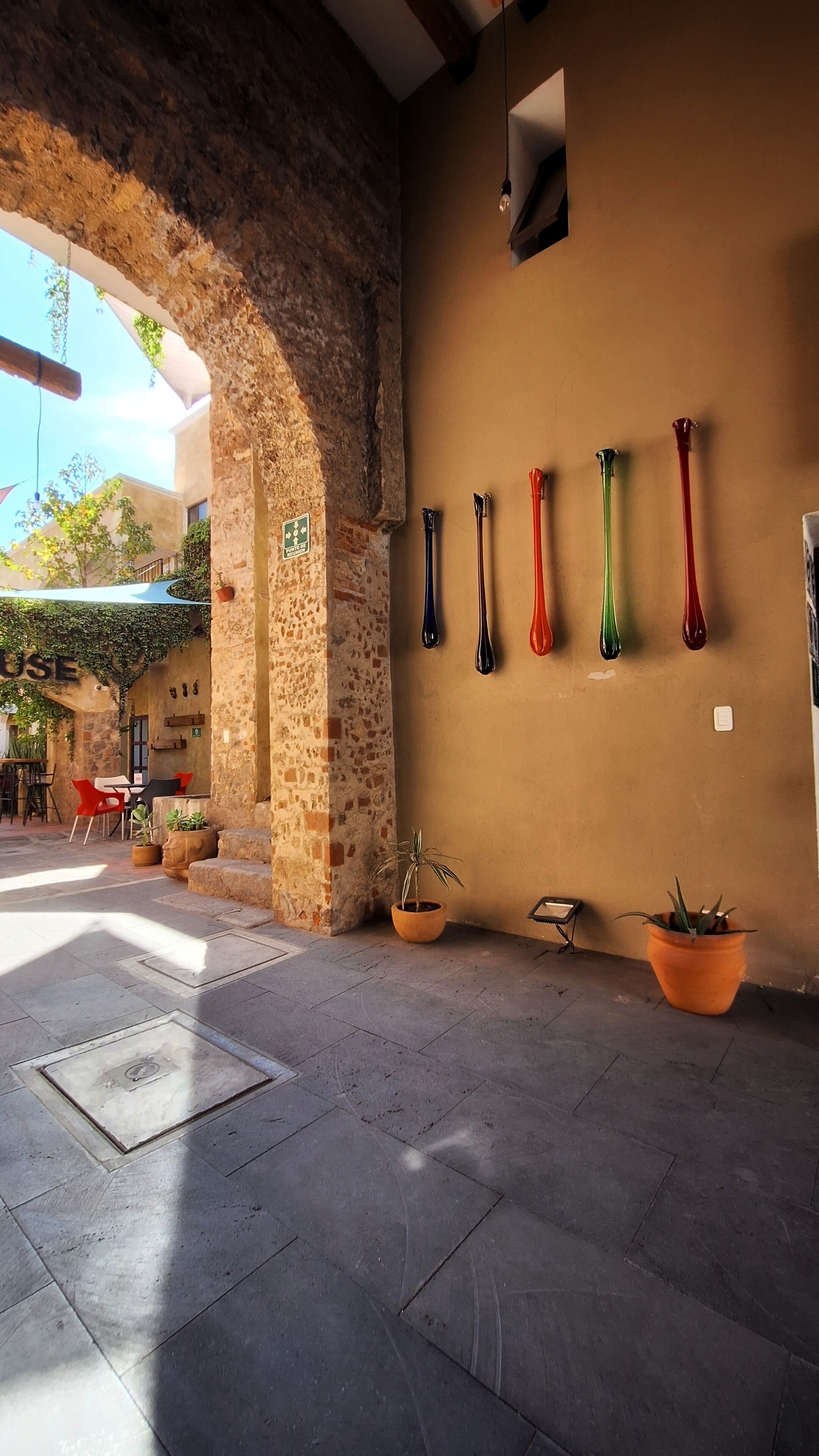 An outdoor area with a stone archway, a wall with vases, and potted plants.