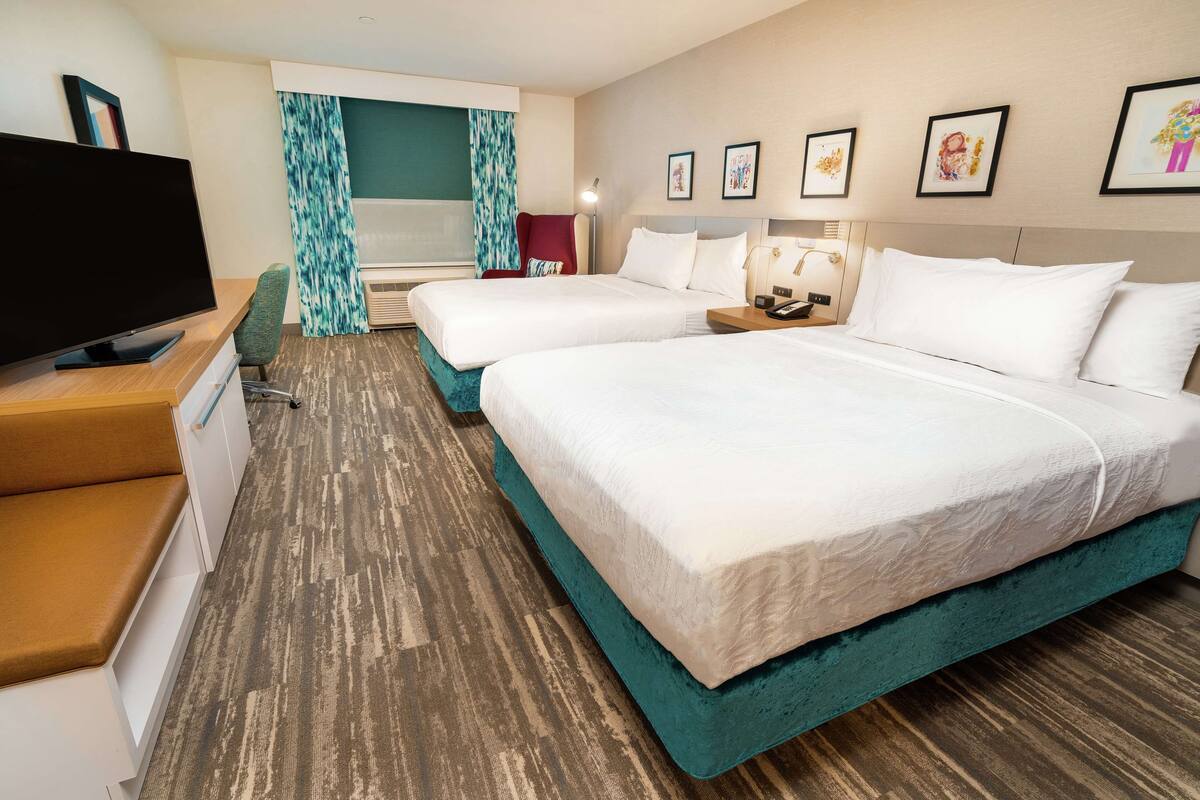 A hotel room with two beds, a TV, a desk, and a chair.
