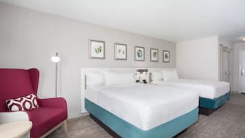 Habitación de hotel con una cama grande, un sillón rojo, una mesita y una lámpara de pie. Cuatro cuadros enmarcados decoran la pared sobre la cama.