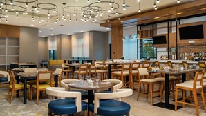 A modern restaurant with round tables, wooden chairs, and a bar area with shelves of bottles. - Hilton Garden Inn Cedar Park Austin (Austin)
