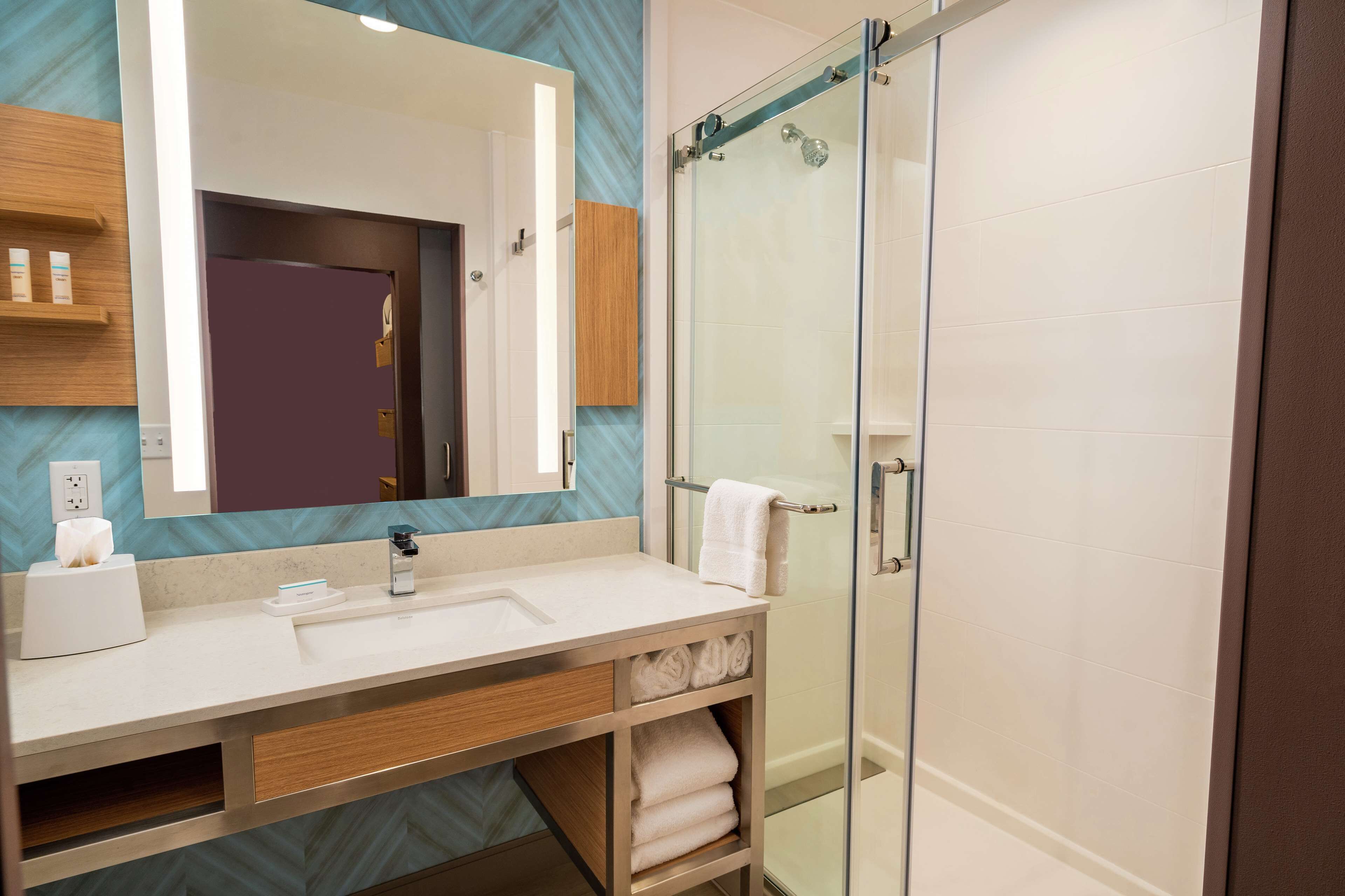 Een moderne badkamer met een douchecabine van glas, een witte wastafel en een spiegel erboven.
