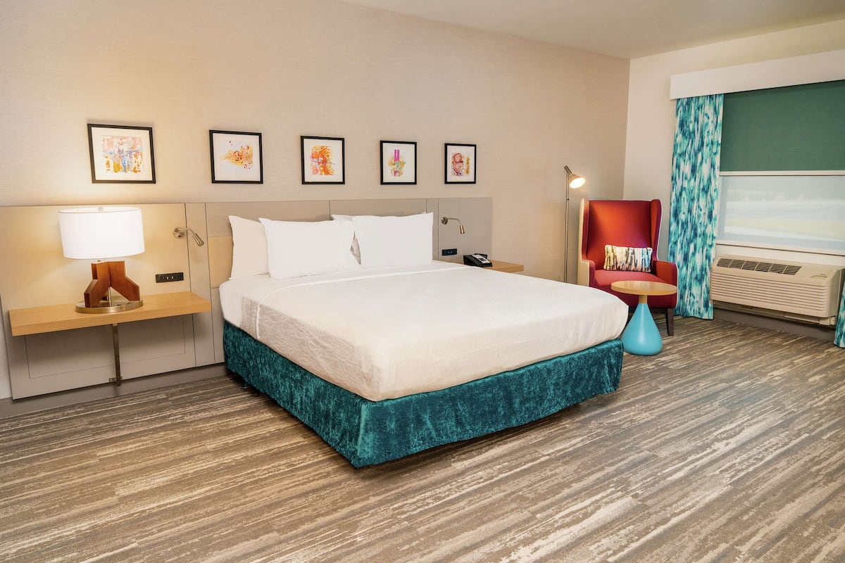 A hotel room with a large bed, a desk, a chair, and a window with curtains.
