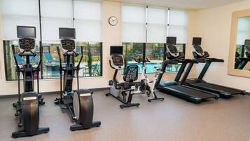A gym with various exercise machines, large windows, and a clock on the wall.