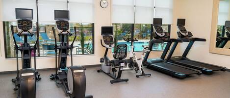 A gym with various exercise machines, large windows, and a clock on the wall.