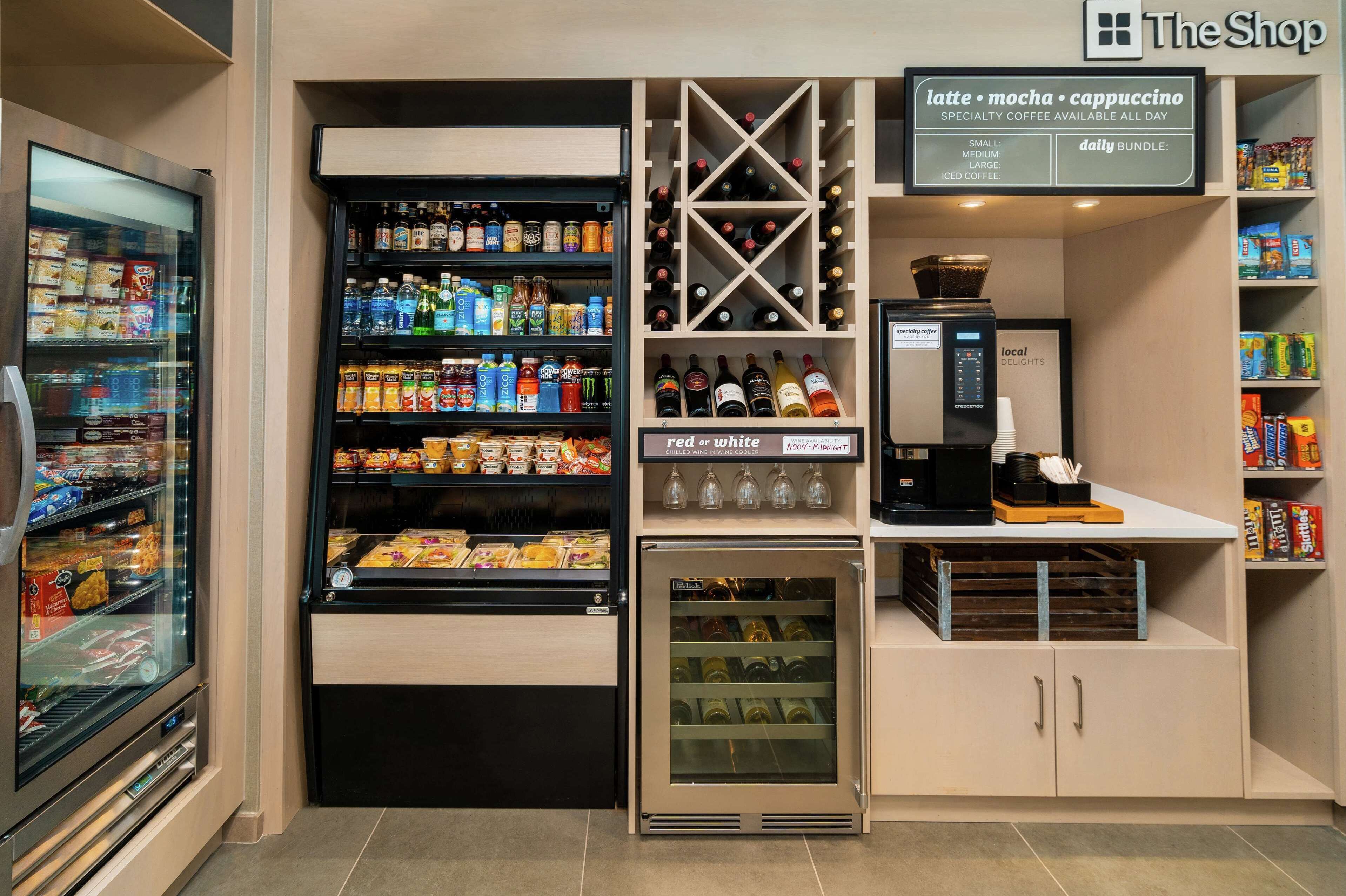 Una cafetería con un mostrador refrigerado, un enfriador de vinos y una máquina de café.