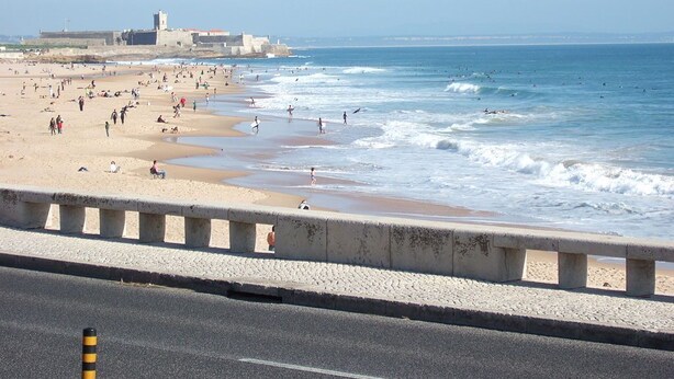 Una playa con una barrera de concreto que separa la carretera de la arena.