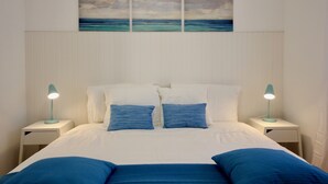Un dormitorio con cama, dos mesitas de noche, un cuadro en la pared y una ventana con persianas.
