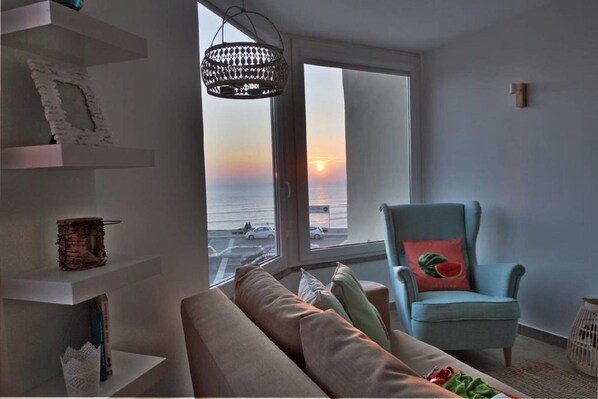 Ein Wohnzimmer mit Meerblick bei Sonnenuntergang, ein blauer Sessel und eine moderne Pendelleuchte.