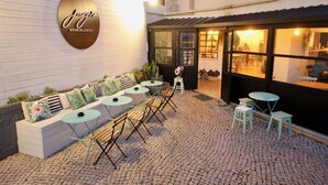 Un área de estar al aire libre con sofá, mesas y sillas, un letrero que dice 'Jezza Brunch & Caffe' y piso de adoquines.