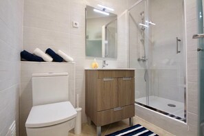 Ein modernes Badezimmer mit Toilette, einem Holzwaschtisch, einer Duschkabine aus Glas und einem Streifen Teppich.