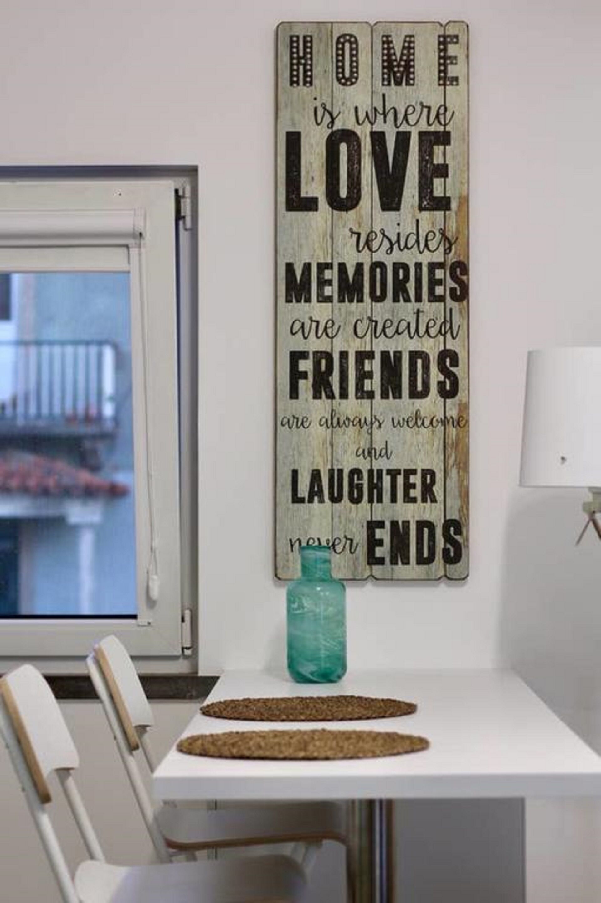 A dining area with a white table and chairs, a decorative sign with a heartfelt message, and a teal vase on the table.