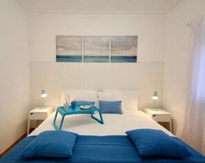 Ein Schlafzimmer mit einem Bett, zwei Nachttischen, einem blauen Beistelltisch und einem Bild über dem Bett.