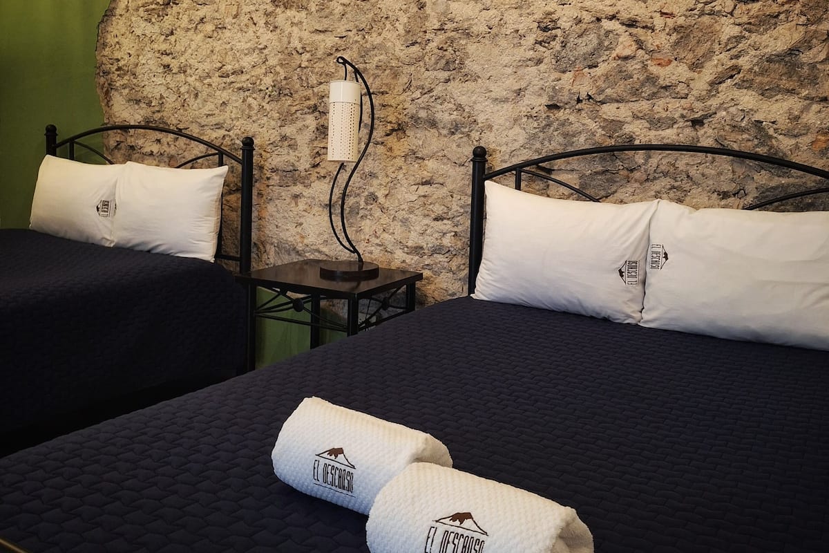 A room with two beds, a stone wall, and a sign with utensils.