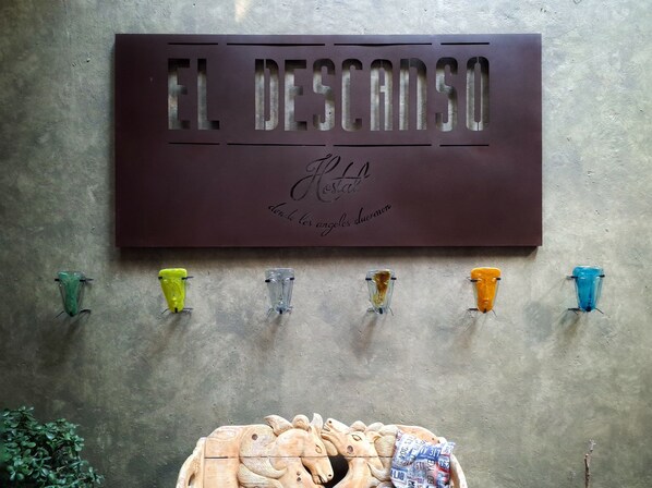 A sign reading "EL DESCANSO" with a logo and text below it. Below the sign, there are six colorful objects hanging on the wall.