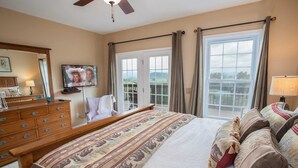 A bedroom with a large bed, a wooden dresser, a television, and a view of the outdoors through a sliding door. - Blue Ridge View Cabin: Hot Tub, Pool Table, Pet-Friendly, Near Blowing Rock & Parkway (Boone)