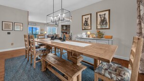 A dining area with a large wooden table, benches, and chairs. There are framed pictures on the walls and a chandelier above the table. - Blue Ridge View Cabin: Hot Tub, Pool Table, Pet-Friendly, Near Blowing Rock & Parkway (Boone)