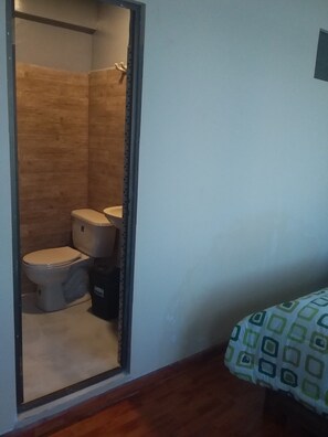A small bathroom with a wooden shower enclosure, a toilet, and a trash bin. - Hotel Nichkito (Uyuni)
