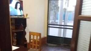 A narrow hallway with a wooden floor, a wooden chair, a small table with a remote control, and a television on a shelf. - Hotel Nichkito (Uyuni)