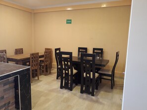 A dining area with a table and chairs, a sign on the wall, and a door. - Hotel Nichkito (Uyuni)