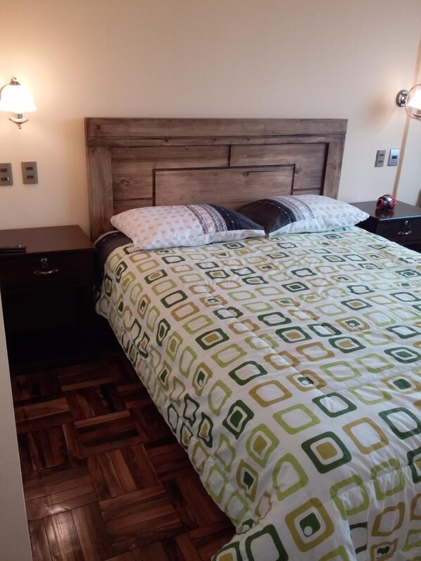 A neatly made bed with a patterned bedspread, a wooden headboard, and two bedside lamps.