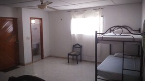 Ein Zimmer mit Etagenbett, Deckenventilator, Stuhl, Fenster mit Vorhängen und einer Tür.