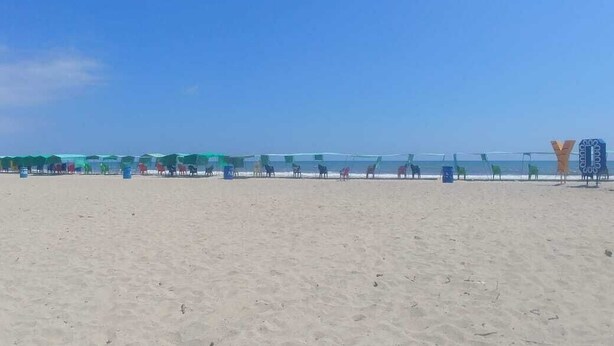 Ein Strand mit Reihen von Sonnenschirmen und Liegestühlen, einem klaren Himmel und einem sandigen Ufer.