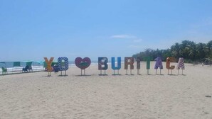 Ein Strand mit bunten Buchstaben, die „BURITACA“ buchstabieren, und einem strahlend blauen Himmel.