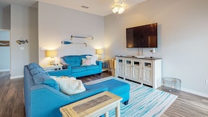Ein Wohnzimmer mit einem blauen Sofa, einem Holztisch, einem Fernseher und einer Vitrine.