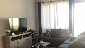 Moderni olohuone, jossa on litteänäyttöinen televisio, harmaa sohva, sohvapöytä ja puinen kaappi.