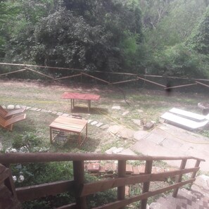 Ein Außenbereich mit einer Holzbank, einem kleinen Tisch und einem roten Tisch. Auf dem Boden liegen Steine und ein Gartenschlauch.