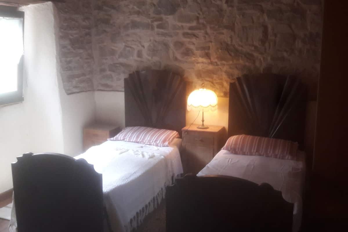 Ein Zimmer mit zwei Betten, einer Steinsäule, einem Fenster und einer Lampe.