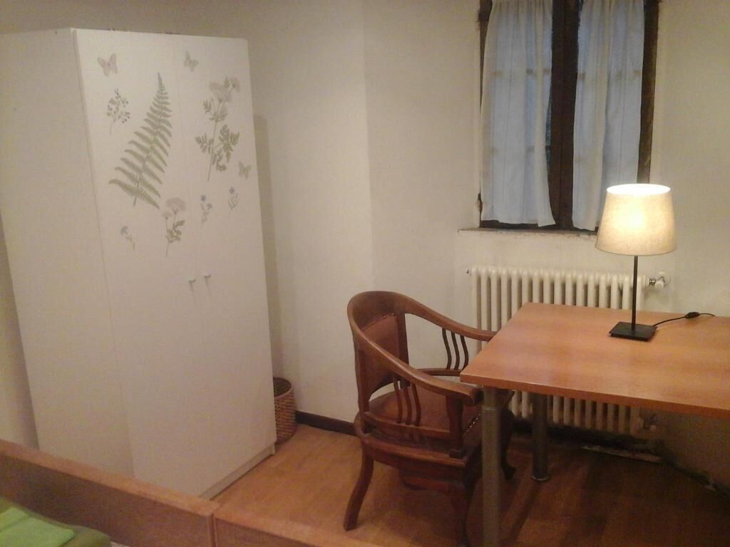 A room with a wooden dining table, a chair, a radiator, and a window with curtains.