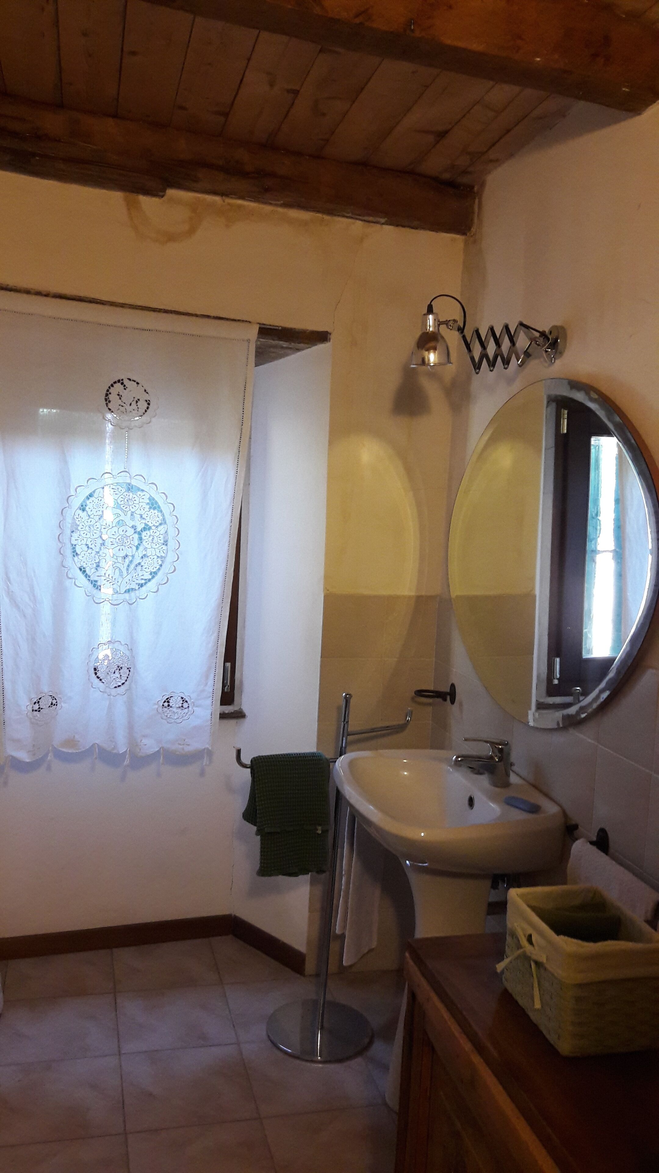 Un baño con un espejo redondo, un lavamanos y un perchero para toallas.