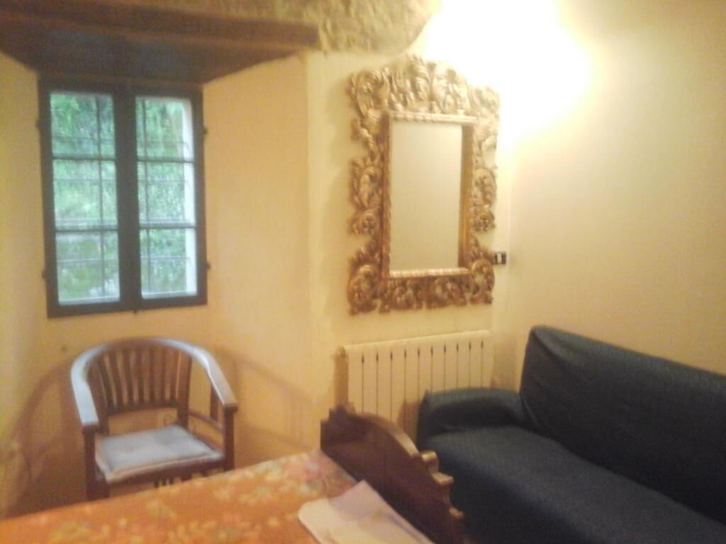 A room with a window, a chair, a sofa, and a mirror on the wall.