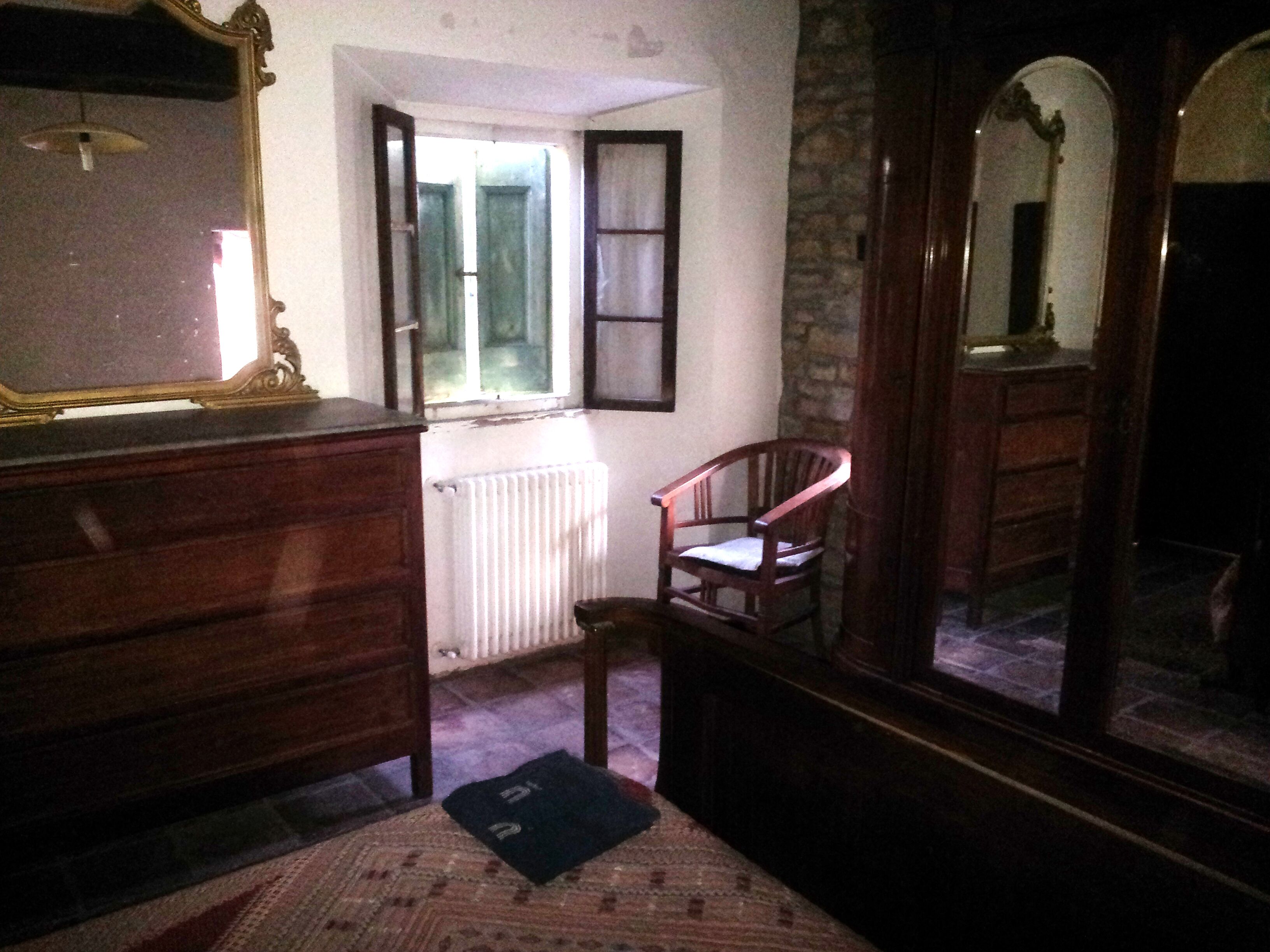 A room with a wooden dresser, a chair, a radiator, and a mirror reflecting part of the room.