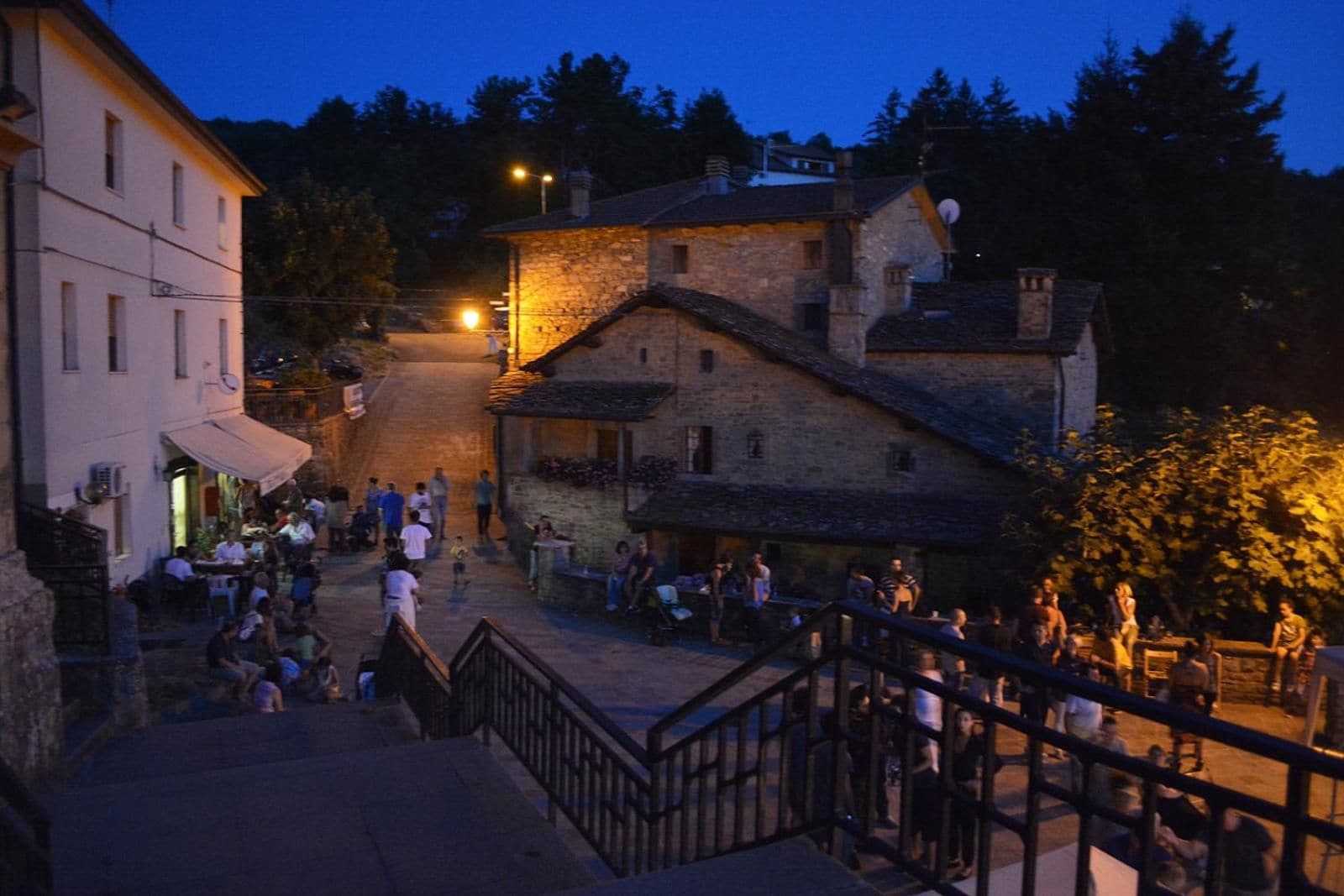A town square with stone buildings, a staircase, and people gathered.