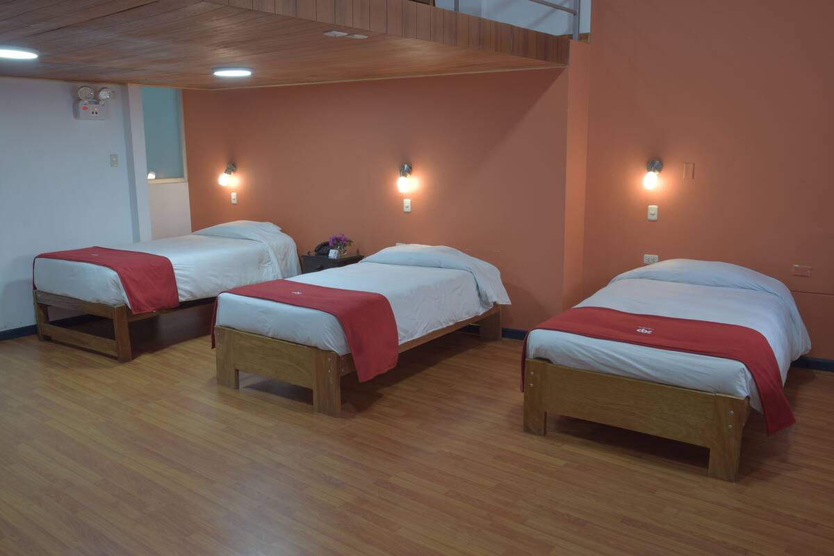 Three single beds with wooden frames and red blankets, wooden floors, and wall-mounted lights.
