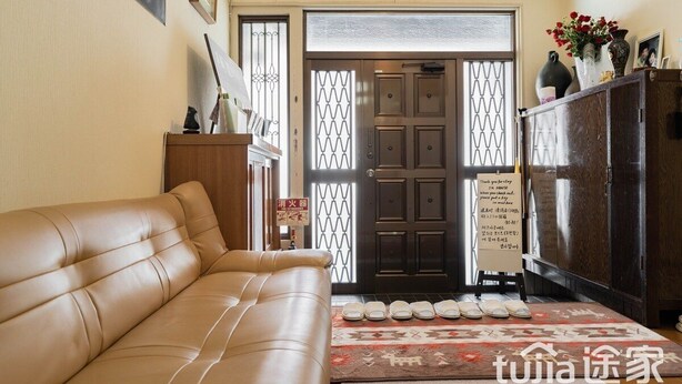 Un salon avec un canapé beige, un meuble en bois et une porte sur laquelle est apposée une pancarte.