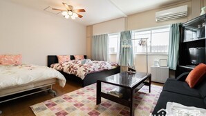 Une chambre d’hôtel avec deux lits, un canapé, une table basse, un ventilateur de plafond, un climatiseur et un téléviseur.