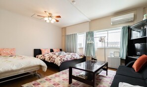 Et hotelværelse med to senge, en sofa, et sofabord, en loftsvifte, en aircondition og et fjernsyn.